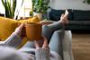 POV of young woman relaxing at home with cup of coffee lying on couch, thinking about blending her retirement savings. Lifestyle concept.