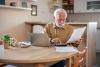 elderly man on laptop in the kitchen, reading papers