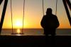 Man alone on a swing looking at empty seat during sunset