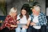 Smiling daughter sitting at home on the sofa with her elderly parents using a laptop and a bank card